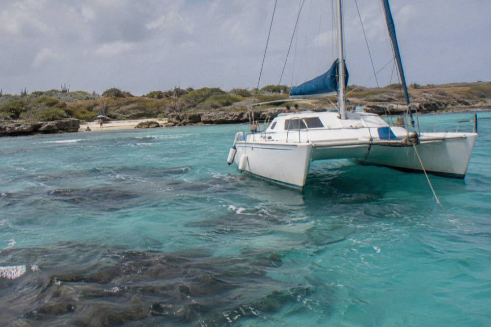 A white catamaran anchored over clear shallow water near a reef on the Aruba coast