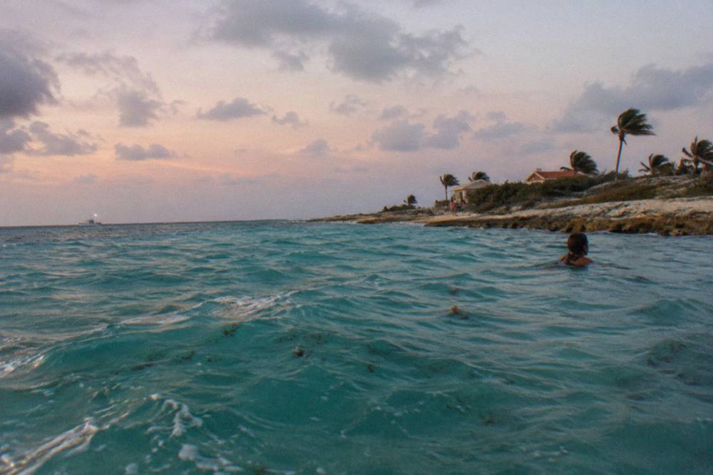 A calm turquoise sea horizon at dusk off the Aruba coastline with scattered clouds