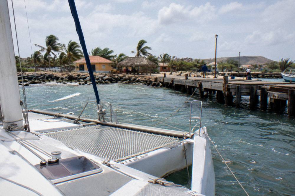 An empty catamaran deck with nets and rigging under a bright sky on calm water