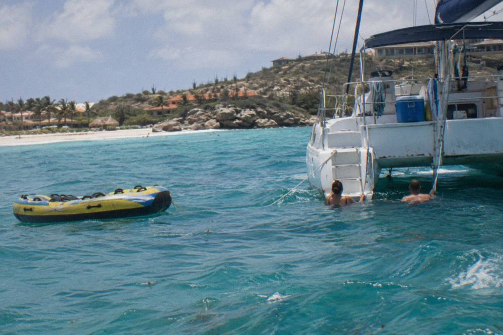 A catamaran anchored over turquoise water with snorkelers beside the hull