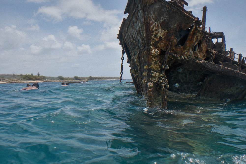 The hull of a sunken ship rising through clear blue water above a reef