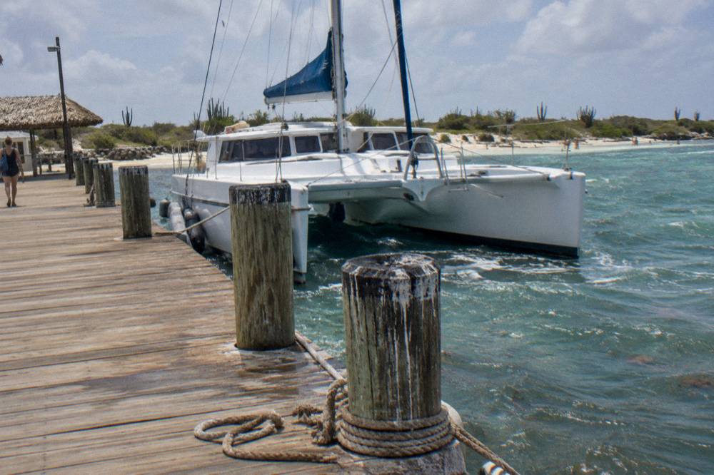A wooden pier extending into calm turquoise water with a catamaran moored nearby
