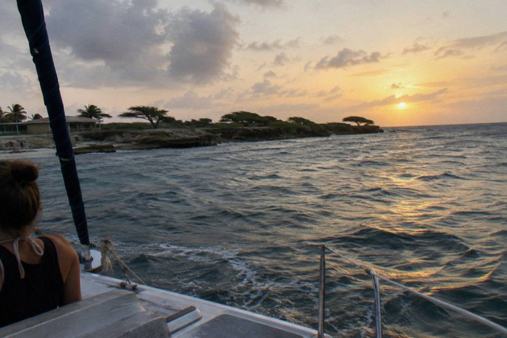 Sun setting over open Caribbean water seen from the deck of a catamaran off the Aruba coast