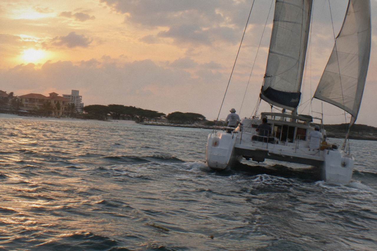 Catamaran sails along the Aruba coast as the sky turns orange over calm water