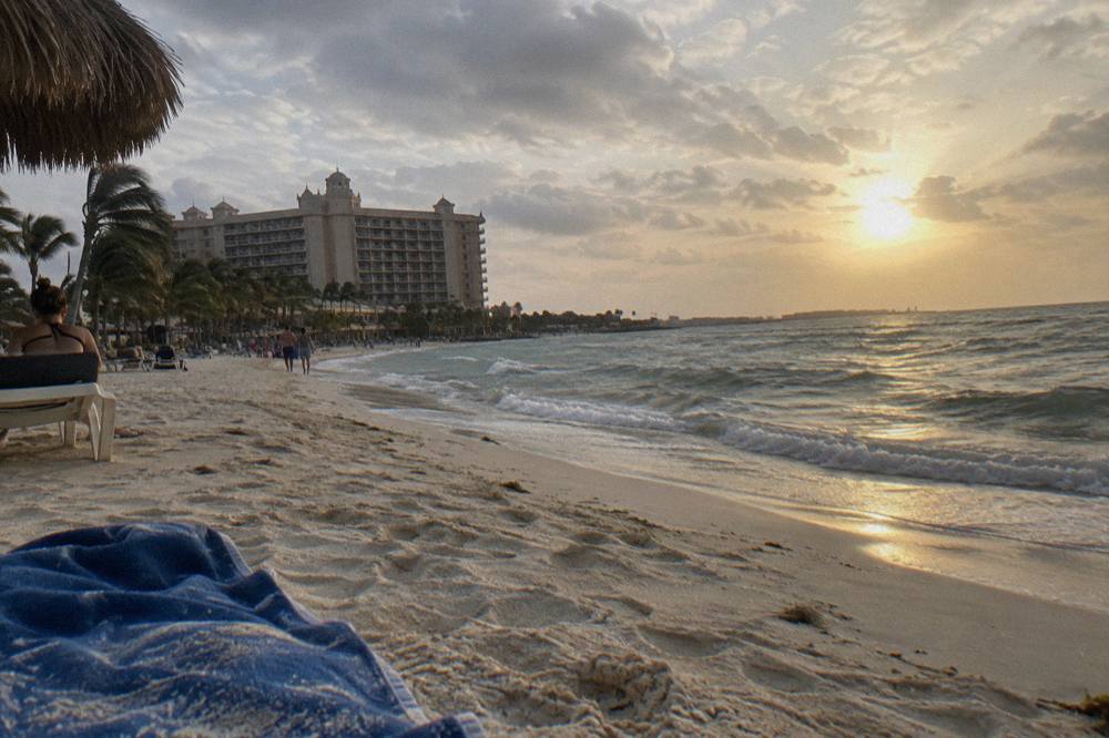 Sun dropping toward the horizon beyond a quiet Caribbean beach with gentle waves
