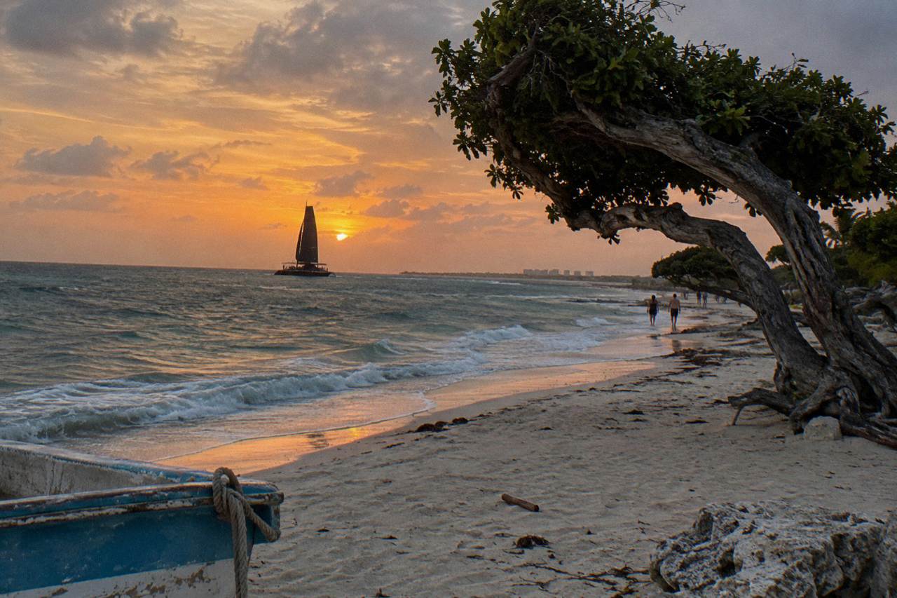 Catamaran sail silhouetted against a wide orange sky over calm Caribbean water