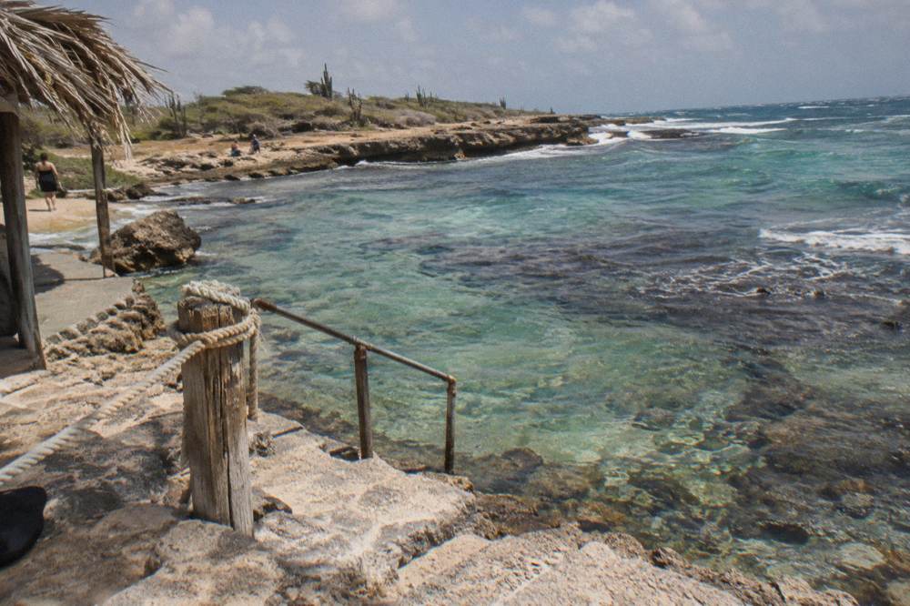 Clear shallow water over coral and rocks near a small rocky beach entry