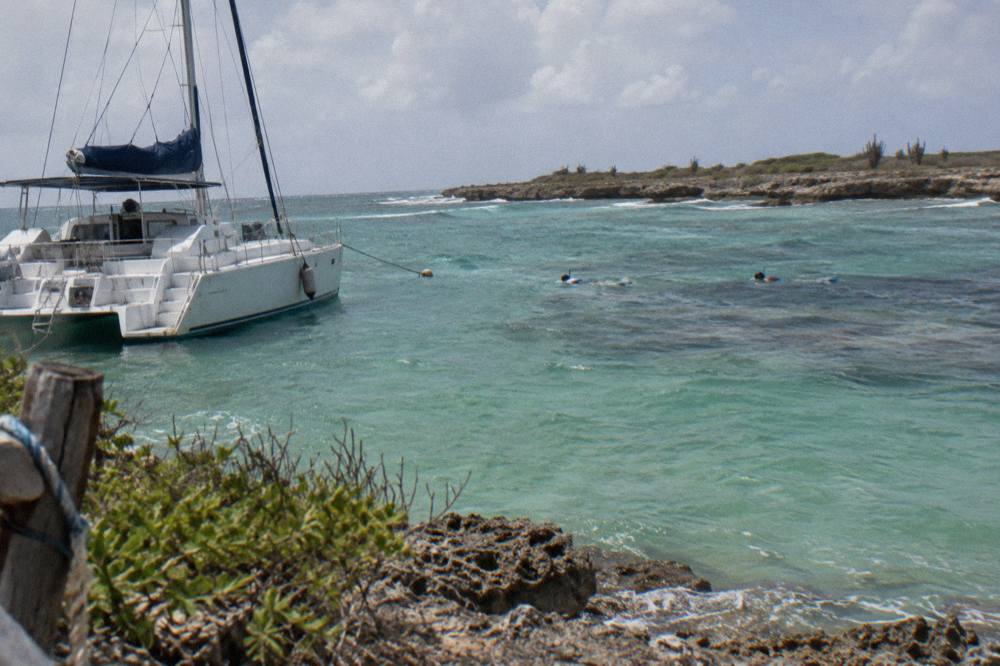 A catamaran moored over clear shallow water with snorkelers visible near a reef