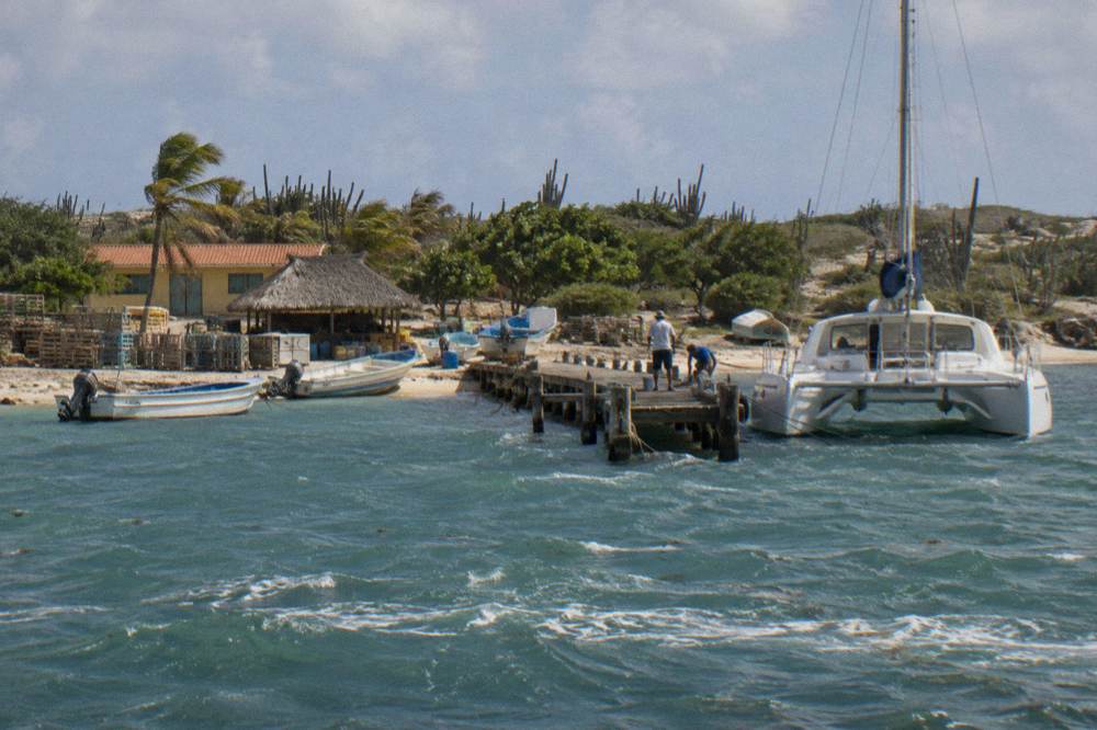 A wooden pier extending into calm blue water with a catamaran at the end