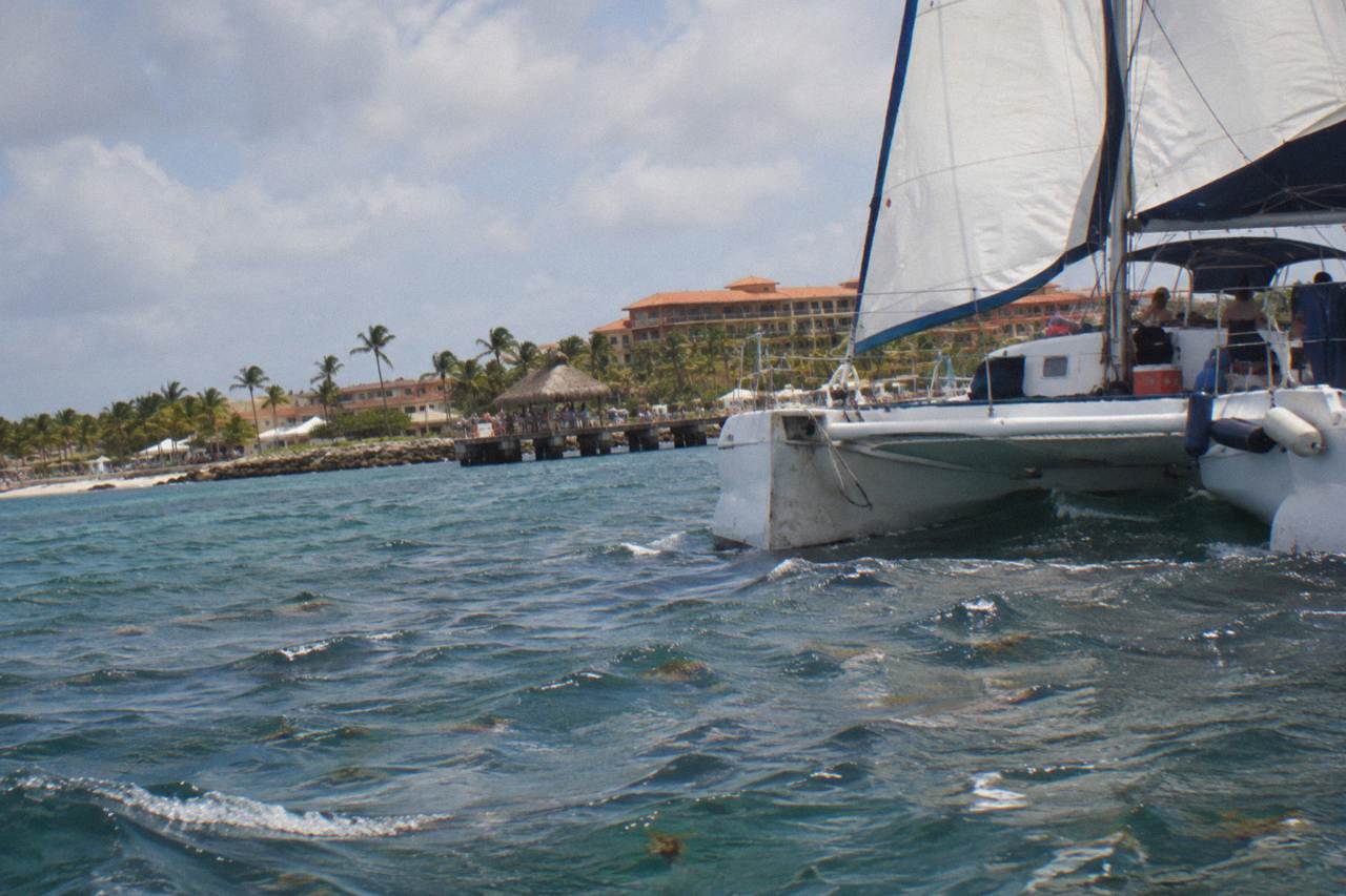A catamaran sailing along the calm turquoise water off the Aruba coast at golden hour