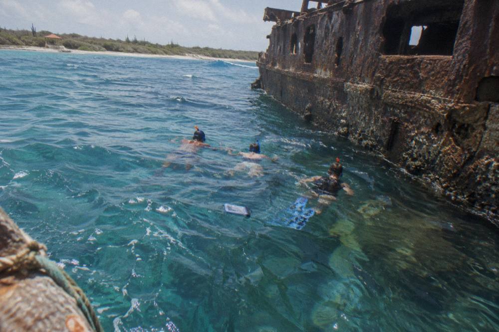 Snorkelers in the water beside a large shipwreck hull in clear blue water