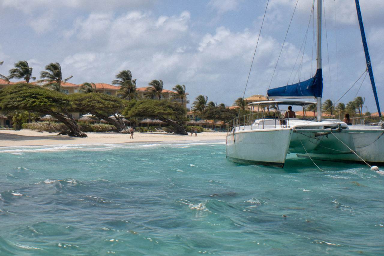White catamaran anchored in clear turquoise water near an Aruba beach