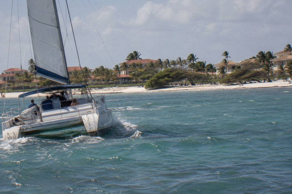 Catamaran under sail off a white sand beach with calm turquoise water