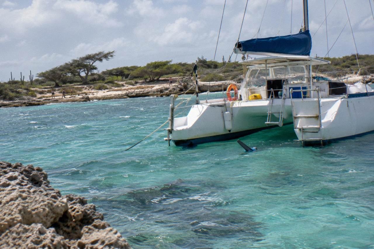 Two-hulled sailing vessel anchored in clear turquoise water near an Aruban beach
