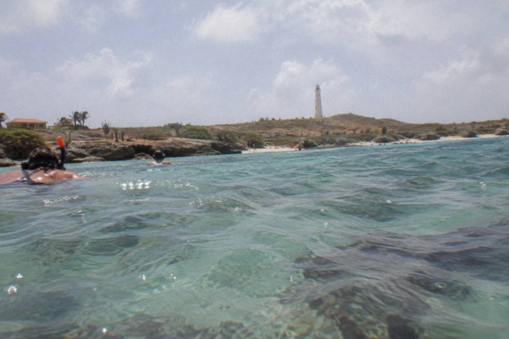 Snorkelers floating in calm clear water above a sandy bay with reef below