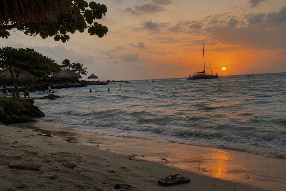 A catamaran silhouetted against an orange sunset over calm Caribbean water