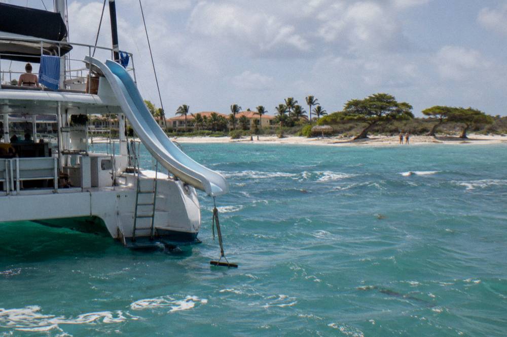 A catamaran at anchor with a water slide and rope swing rigged on the stern