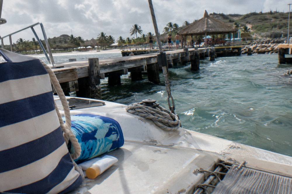 A beach bag towel and sunscreen on the deck of a catamaran beside clear water