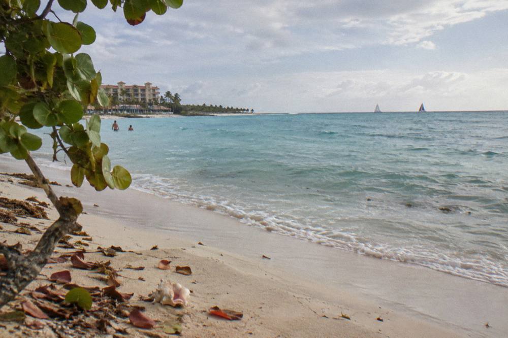 Calm turquoise sea along a sandy shore with a few sails on the horizon