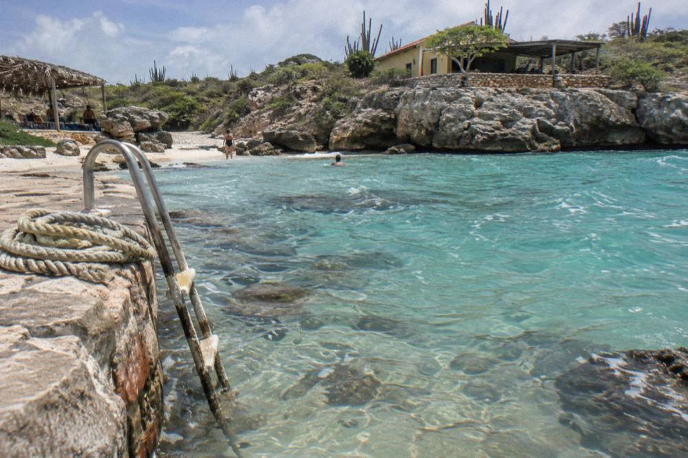 Sheltered rocky cove with clear shallow water over pale sand and scattered smooth rocks