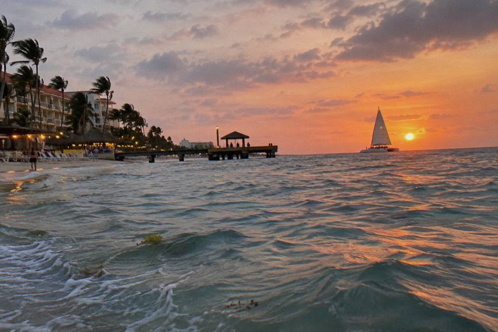 Catamaran sails along the Palm Beach coastline under a pink and orange evening sky