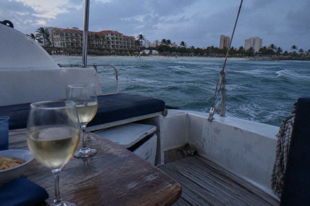 Dinner table set on a catamaran deck with wine glasses at dusk