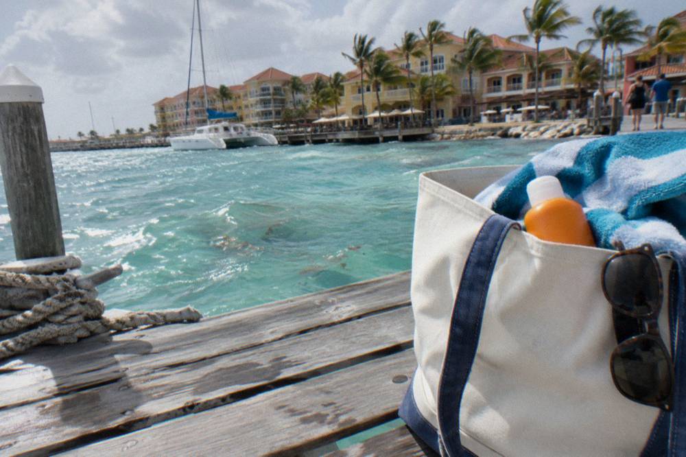Beach bag with towel, sunscreen and sunglasses on a wooden dock beside a boat
