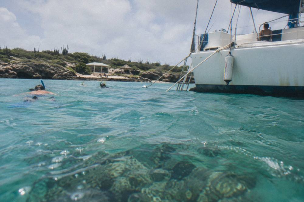 Catamaran anchored over clear shallow water near a coral reef with snorkelers