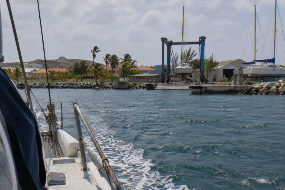 Catamaran underway on calm blue water with a marina and town in the background