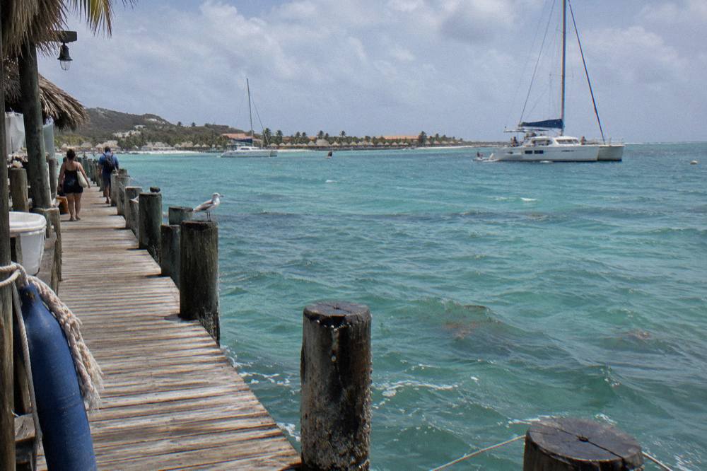 Wooden pier extending over calm turquoise water with catamarans at anchor