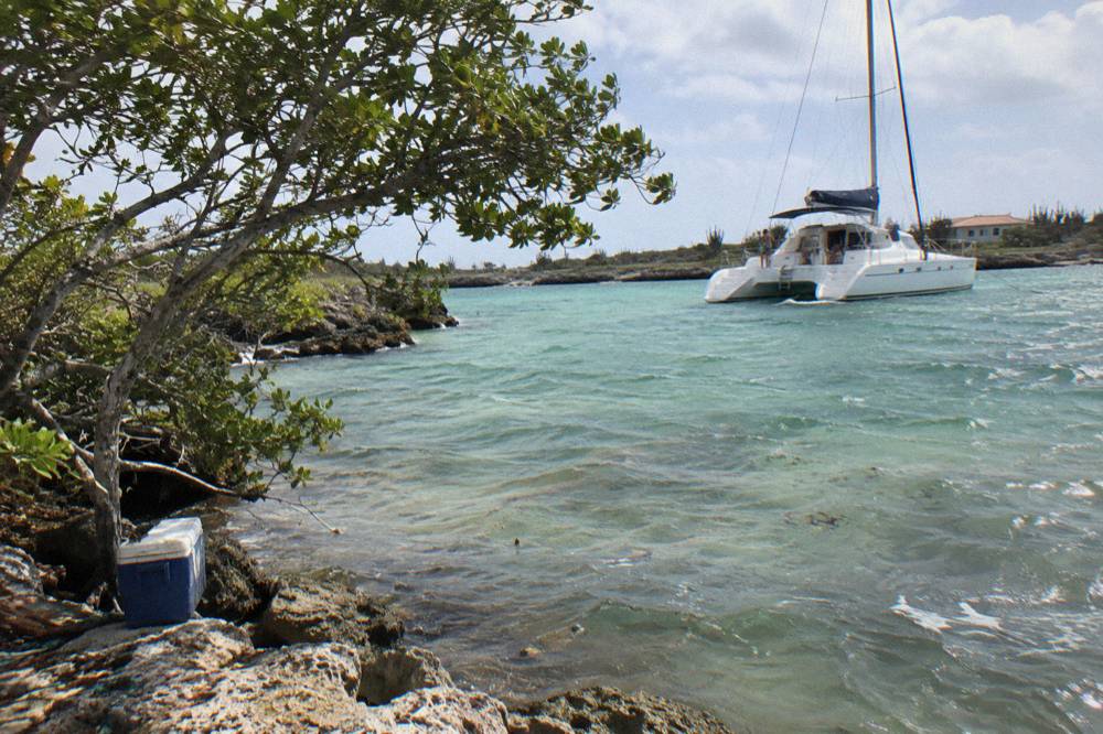 Sailboat catamaran anchored near a rocky shoreline with clear shallow water