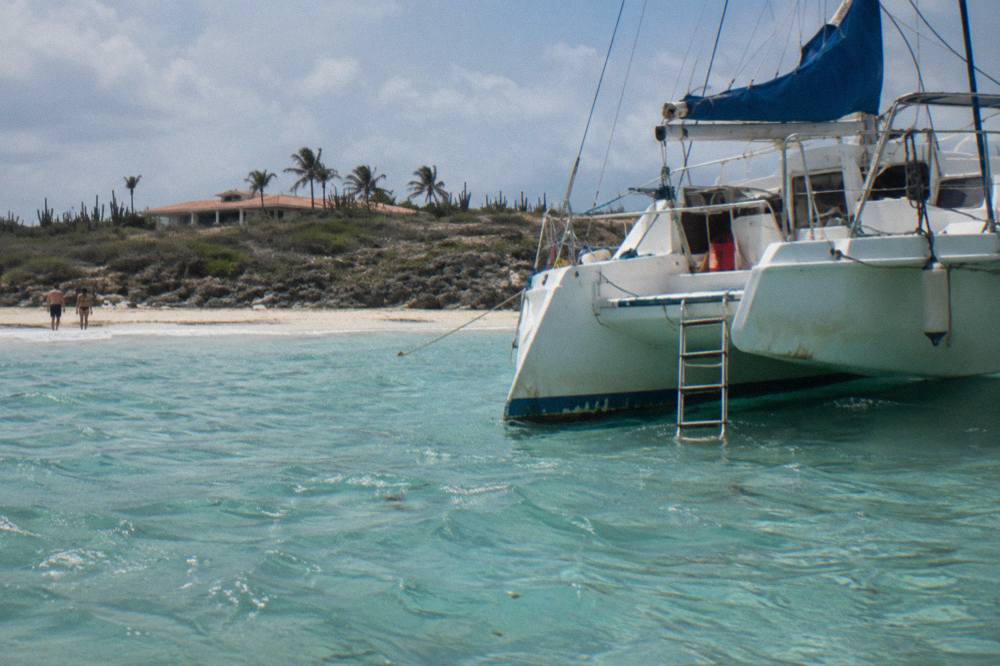 A private catamaran moored beside an empty beach with clear shallow water