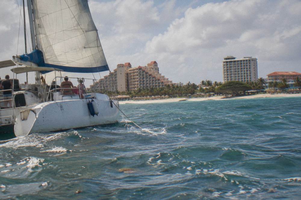 A catamaran under sail near the Aruba coastline in late afternoon light