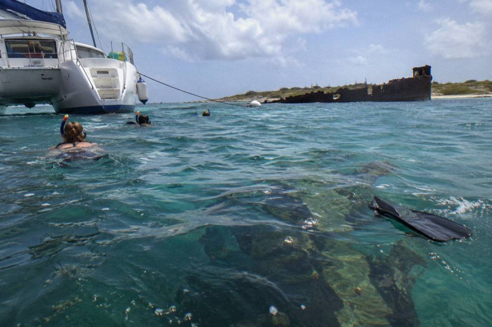 A catamaran moored near a shallow reef with snorkelers visible in clear water beside the boat