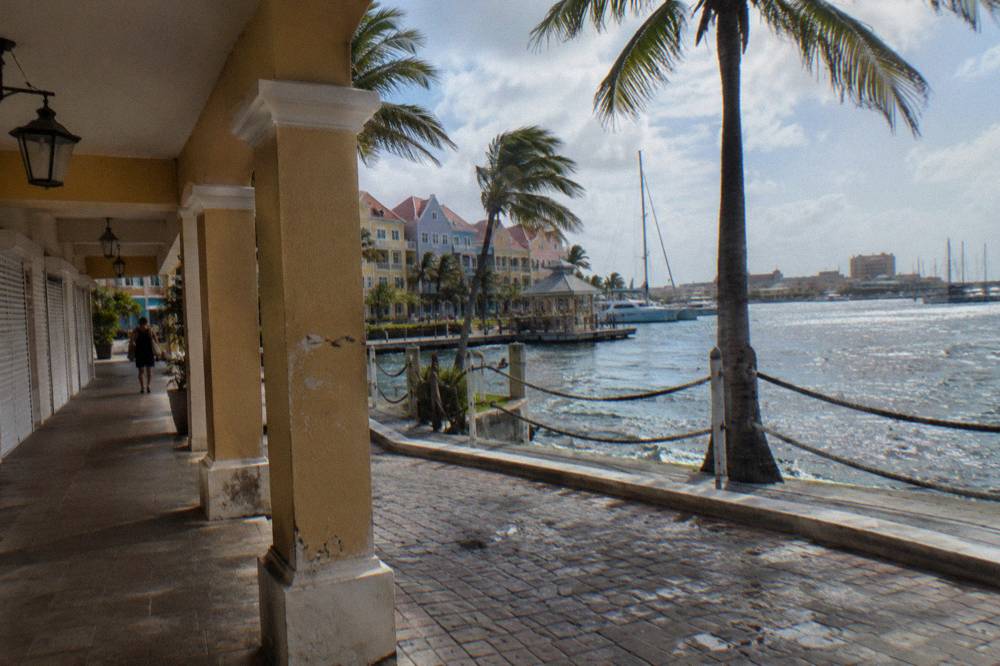 Sunny beach promenade in Aruba with palm trees, shops and calm sea in the background