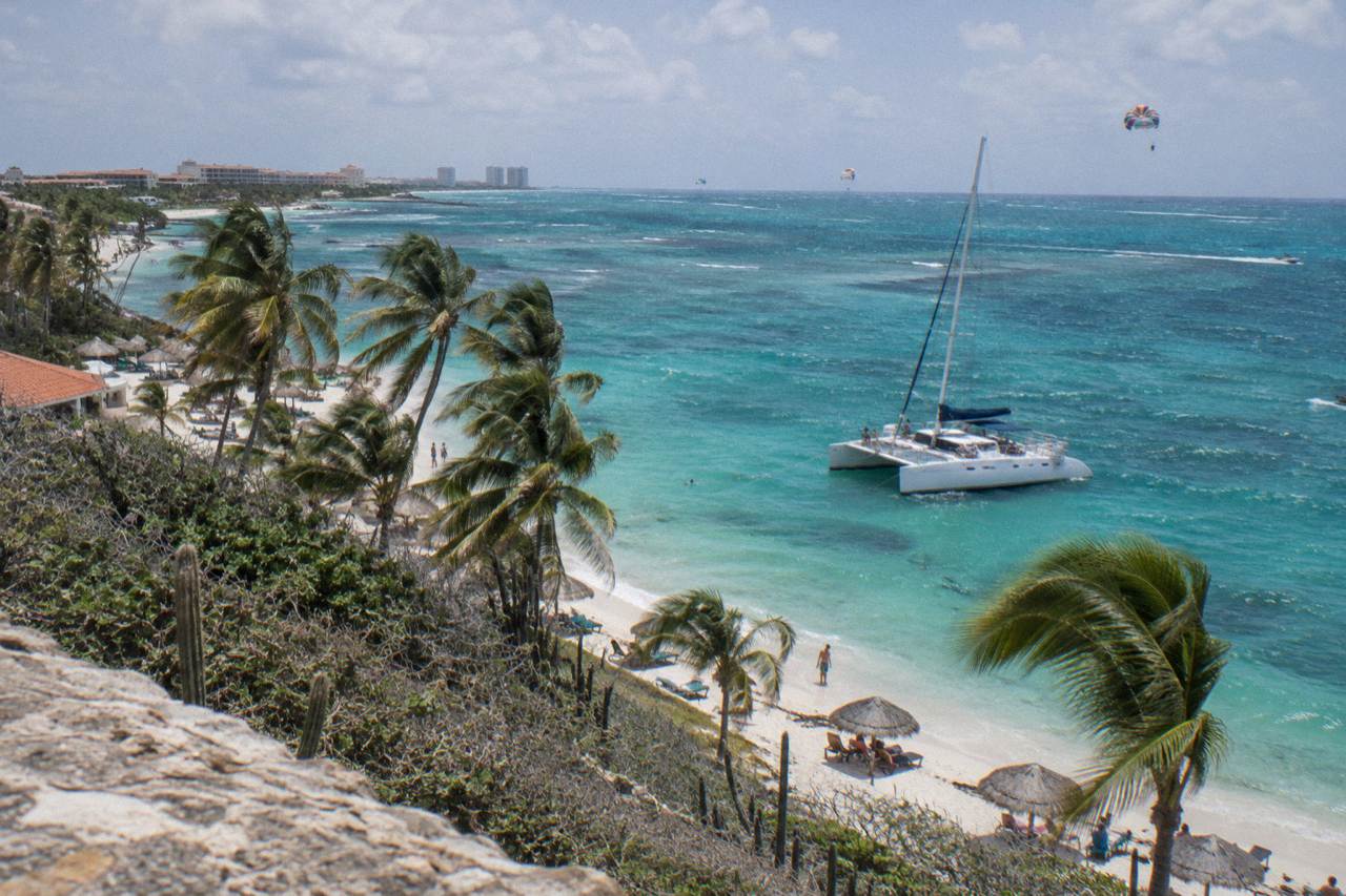 Catamaran anchored in clear turquoise water off an Aruba beach with white sand and palm trees