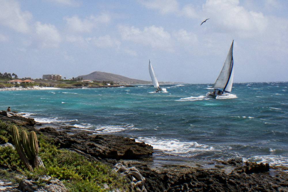 Sailboat and catamaran sails on blue Caribbean water under scattered clouds