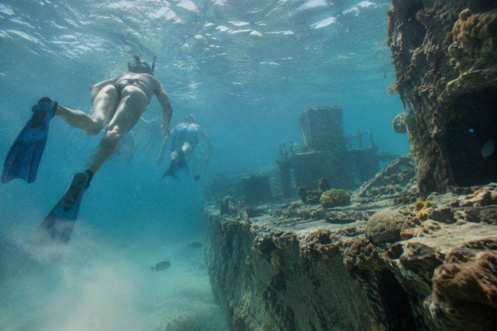 Snorkelers in calm water above a coral reef with a catamaran anchored behind