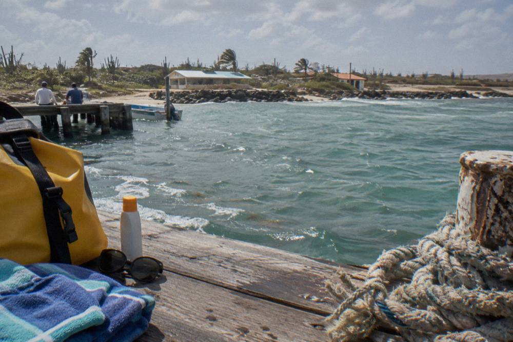 A dry bag, towel, sunglasses and sunscreen bottle arranged on a wooden dock beside mooring lines