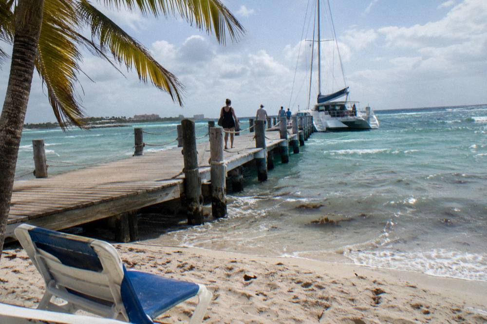 A wooden pier extending into calm turquoise water with a moored catamaran at the end