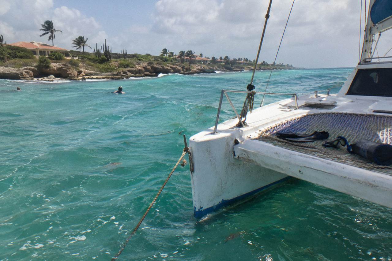 A catamaran anchored in clear turquoise water off the Aruban coast with snorkel gear laid out on the deck