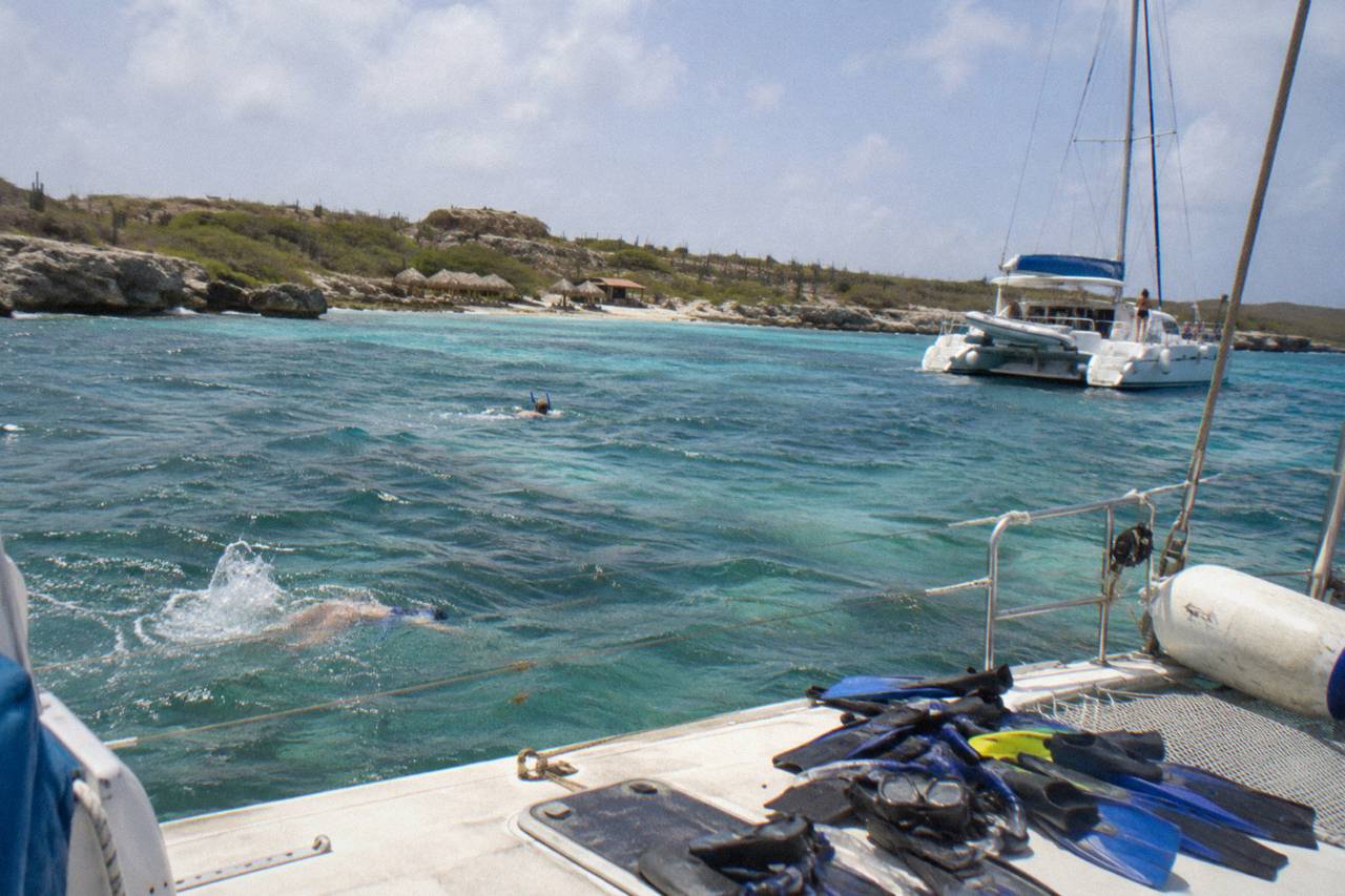 Catamaran at anchor over a pale reef shelf at Boca Catalina, Aruba, with fins and masks on deck